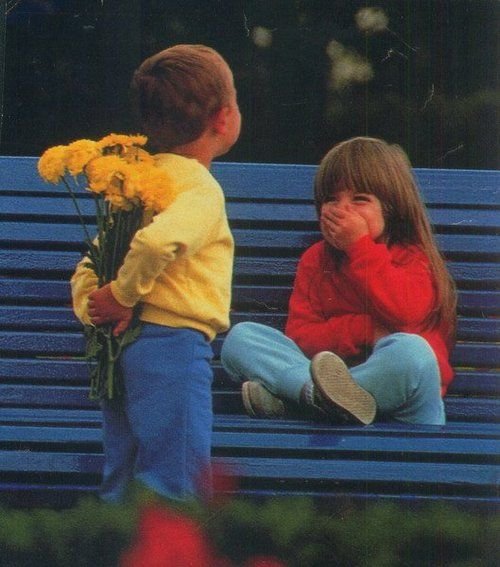 Un niño esconde un ramo de flores para regalárselo a una niña sentada en un banco