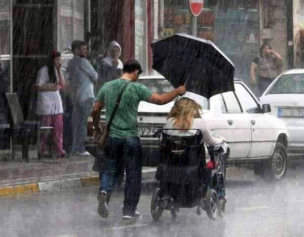 Un hombre protege de la lluvia con su paraguas a una mujer en silla de ruedas